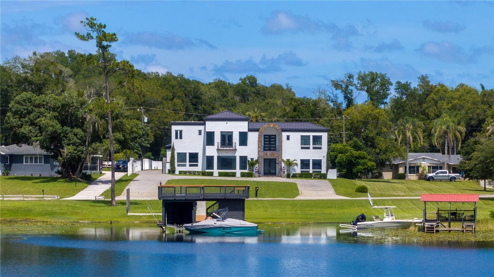 736 Lake Winnemissett Drive seen from the water, with the private boathouse and a wake boat on its lift in front of the residence