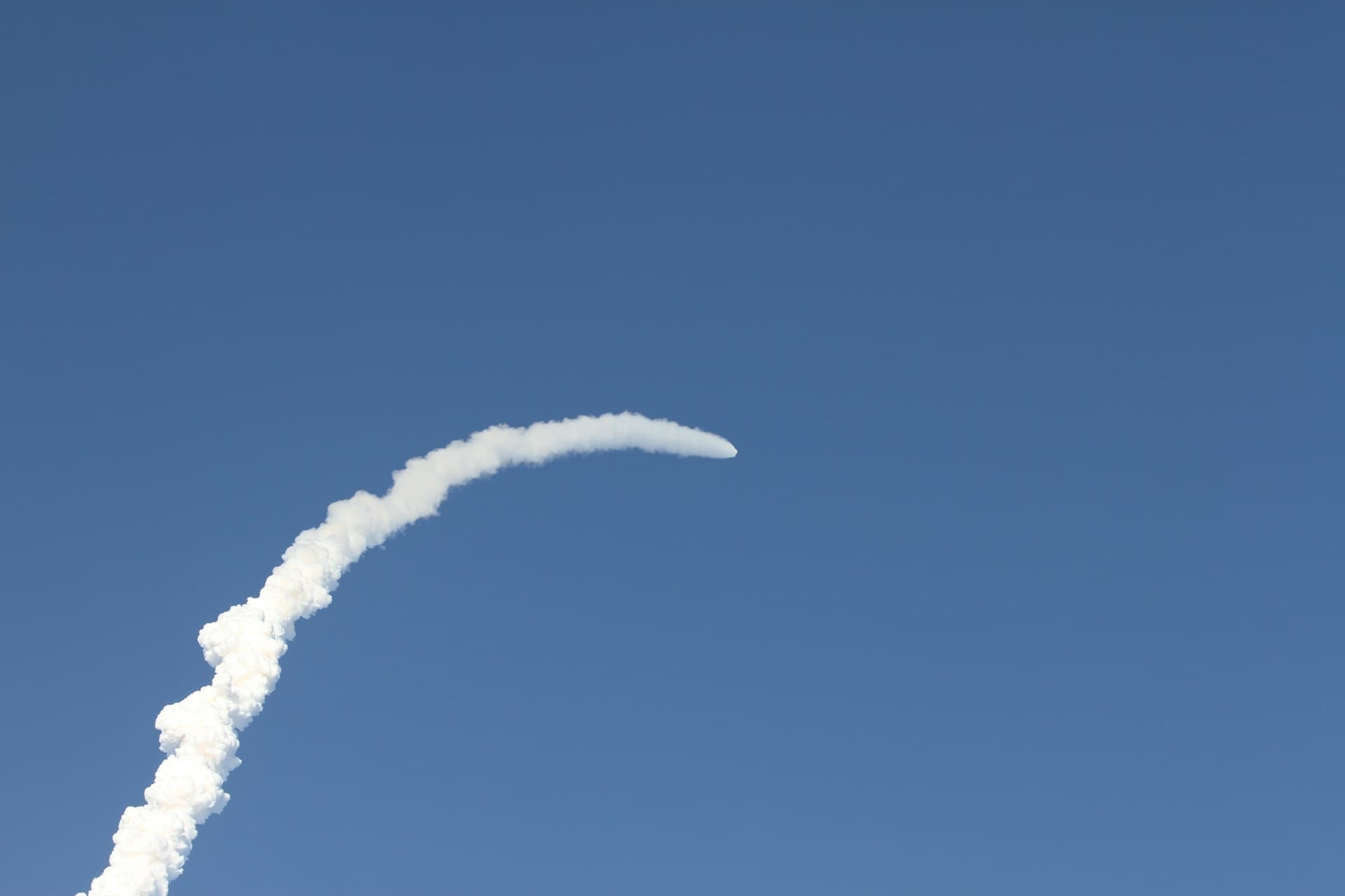 Rocket launch trail arcing across a clear blue Space Coast sky