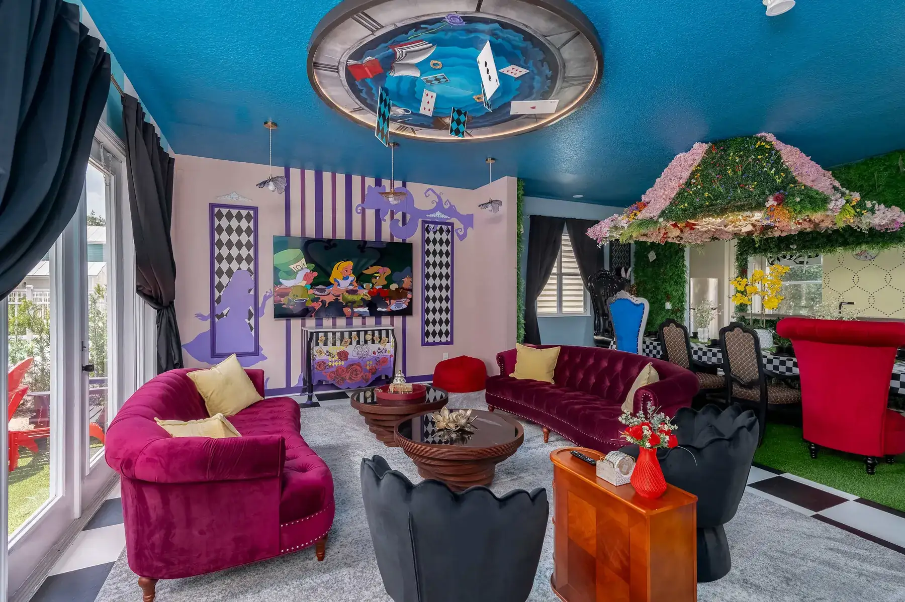 Storybook-themed living room with tufted velvet sofas, a painted tea-party ceiling mural and a floral canopy over the dining nook.