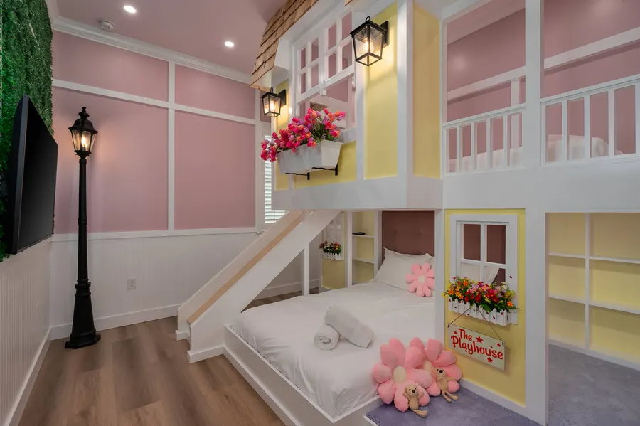 Playhouse-themed bunk bedroom built as a two-story cottage facade, with flower boxes, a street lamp and a staircase to the upper bunk.