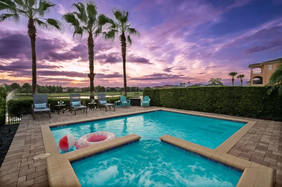 Screened pool and spa at dusk behind a Reunion residence, with loungers, tall palms and the golf course beyond under a violet sky.