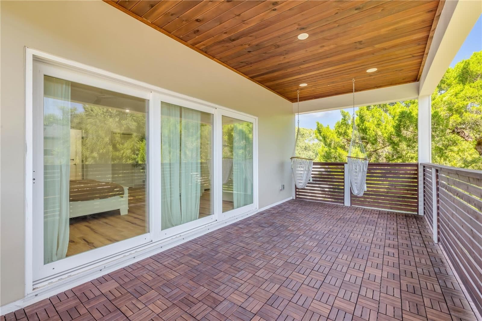 The covered balcony off the primary suite, with a wood ceiling, brick floor and views into the oak canopy